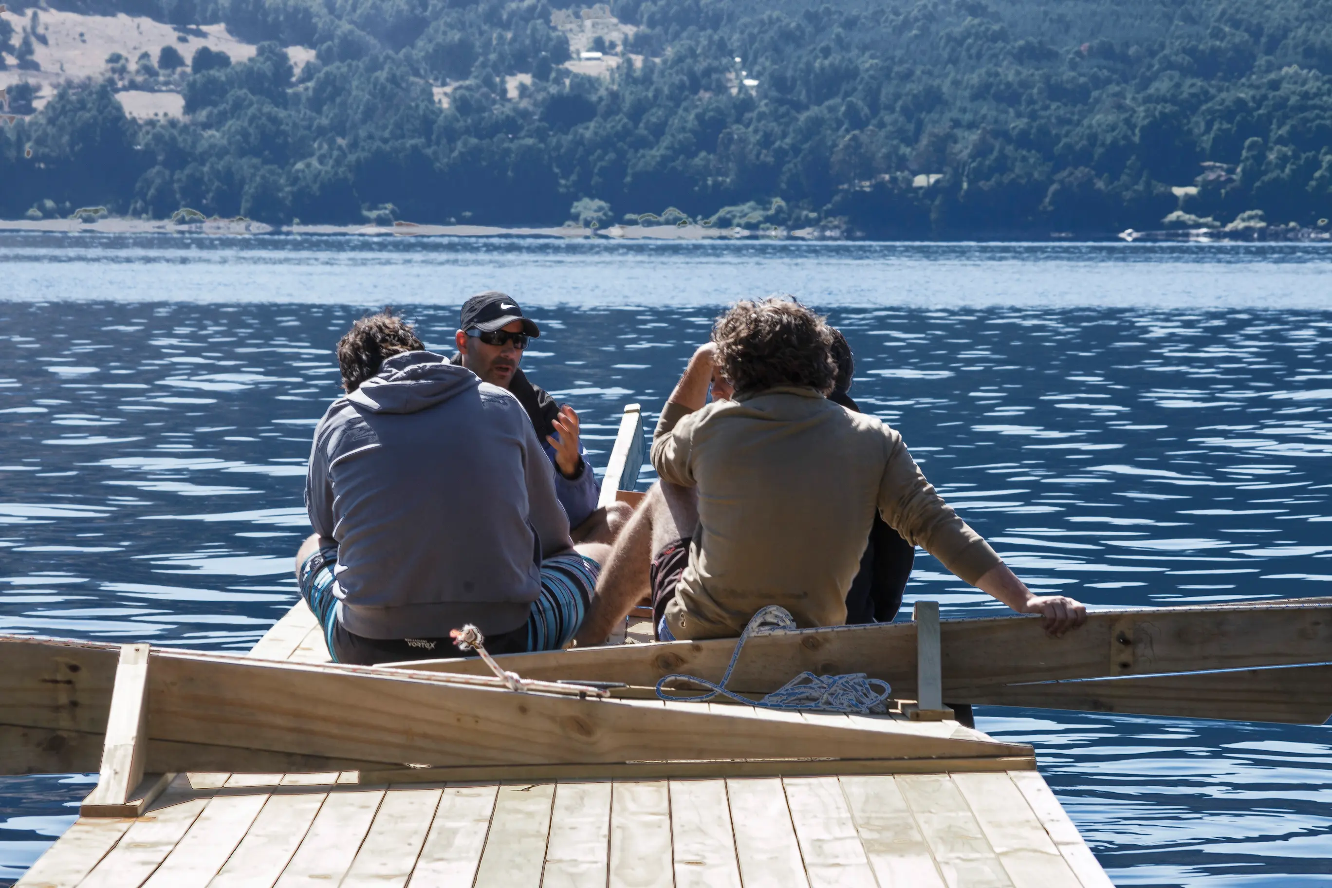 Tres personas conversando sentadas en un bote junto a un muelle