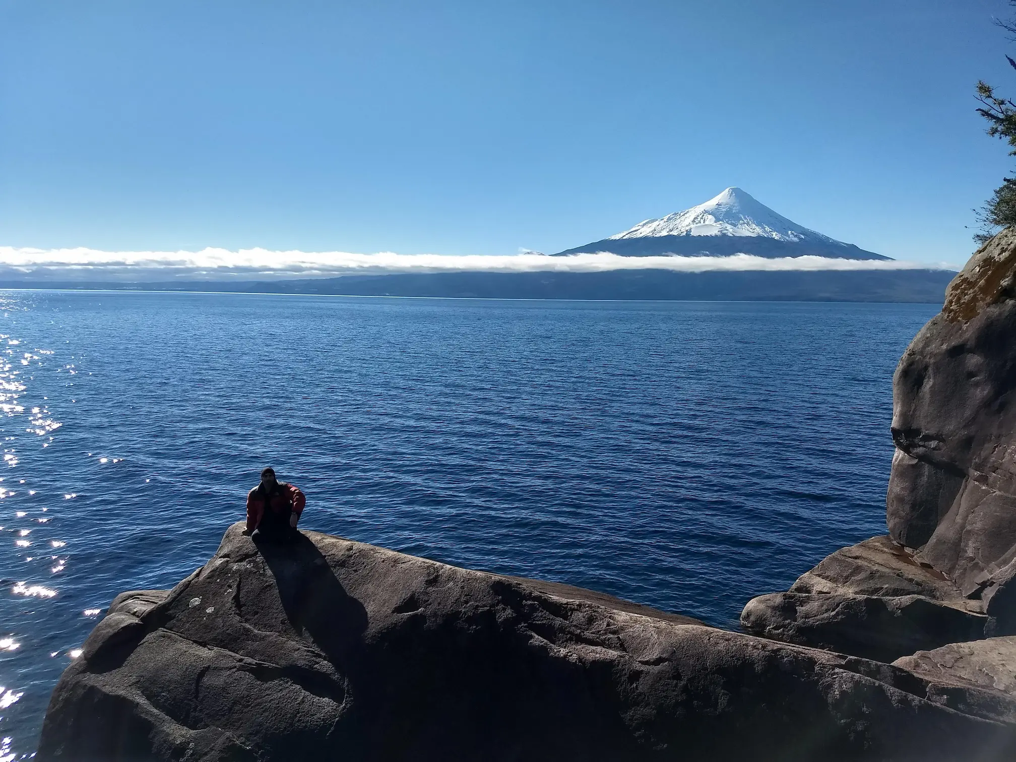 Lago Llanquihue con el volcán Osorno al fondo y una persona sentada sobre las rocas