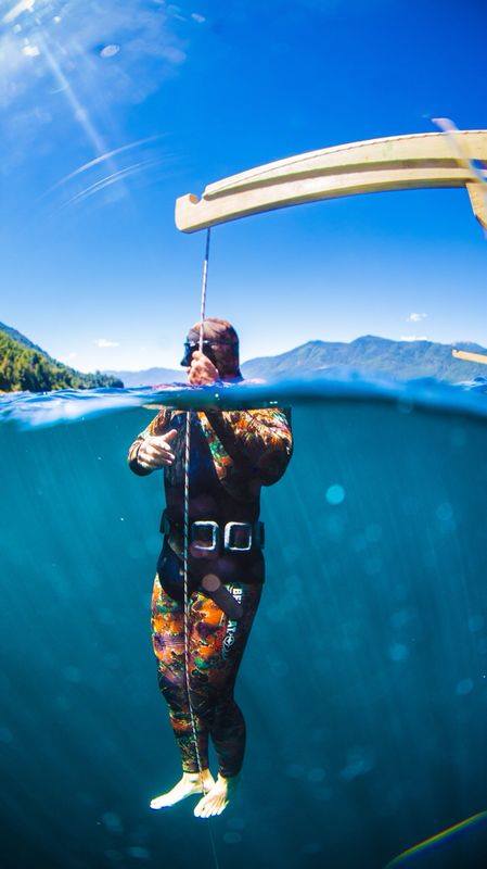Persona en el agua vista mitad sobre y mitad bajo la superficie, con montañas al fondo